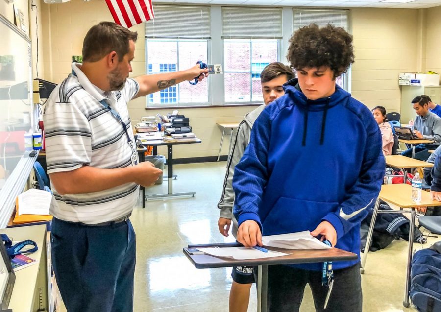 English teacher Jon Karschnik distributes new student IDs with lanyards to his students during one of his classes.     
