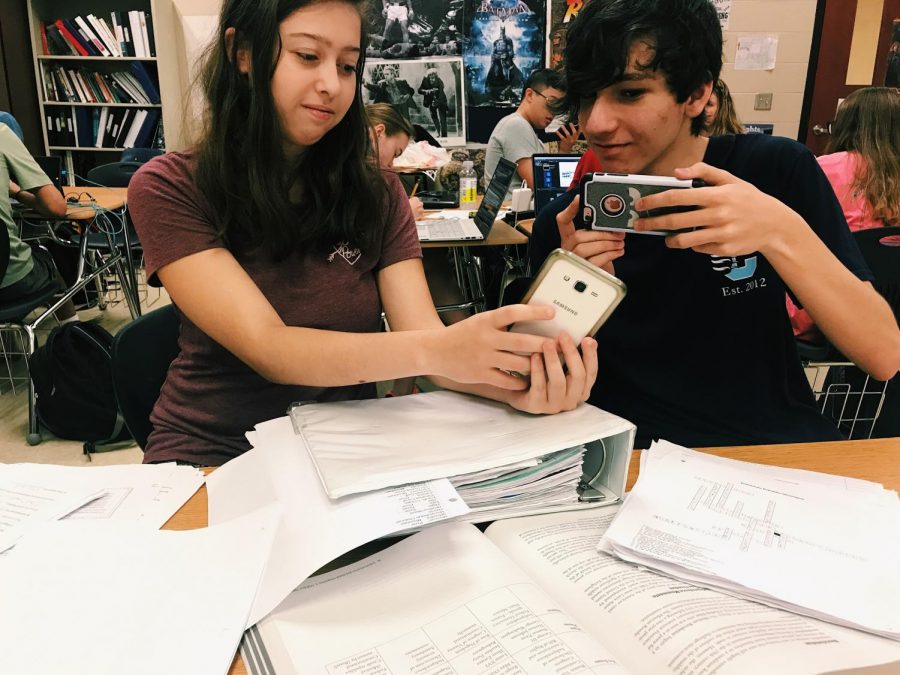 Students Ori Yoked and Lukas Martinson are concentrated on their phones while their papers lie in front of them, waiting to be completed.