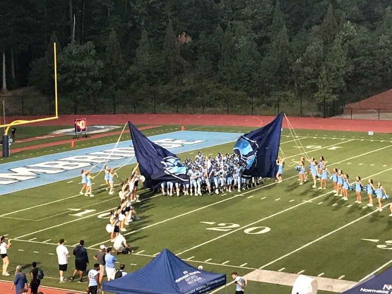 Football players running through the flag at kickoff.