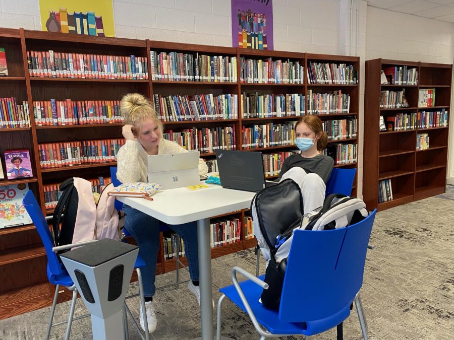 Students study in the library, one with a mask and one maskless.